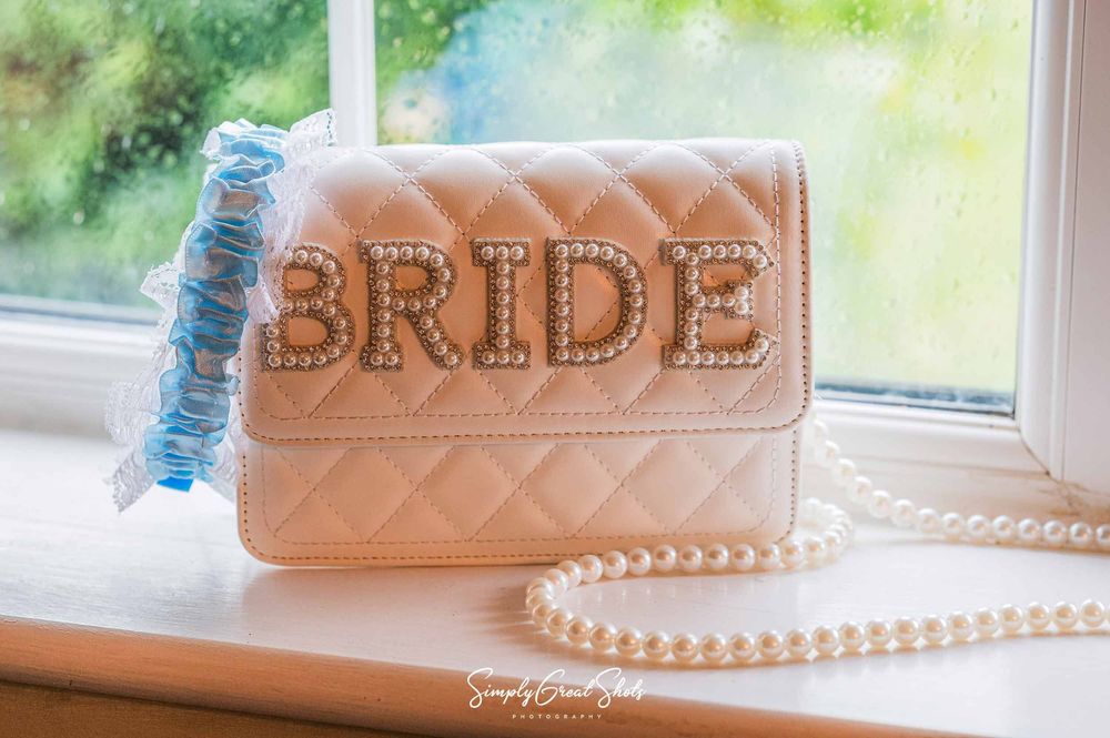 A bridal bag and blue garter photographed next to a window by a Winters Tale Wedding Photographer