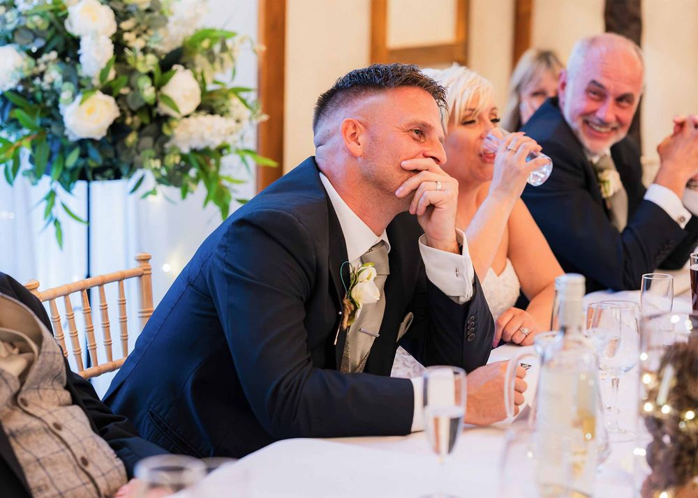 A wedding phtographer captures the top table smiling intently whilst listening to the best mans speech at Winters Tale Country Barn