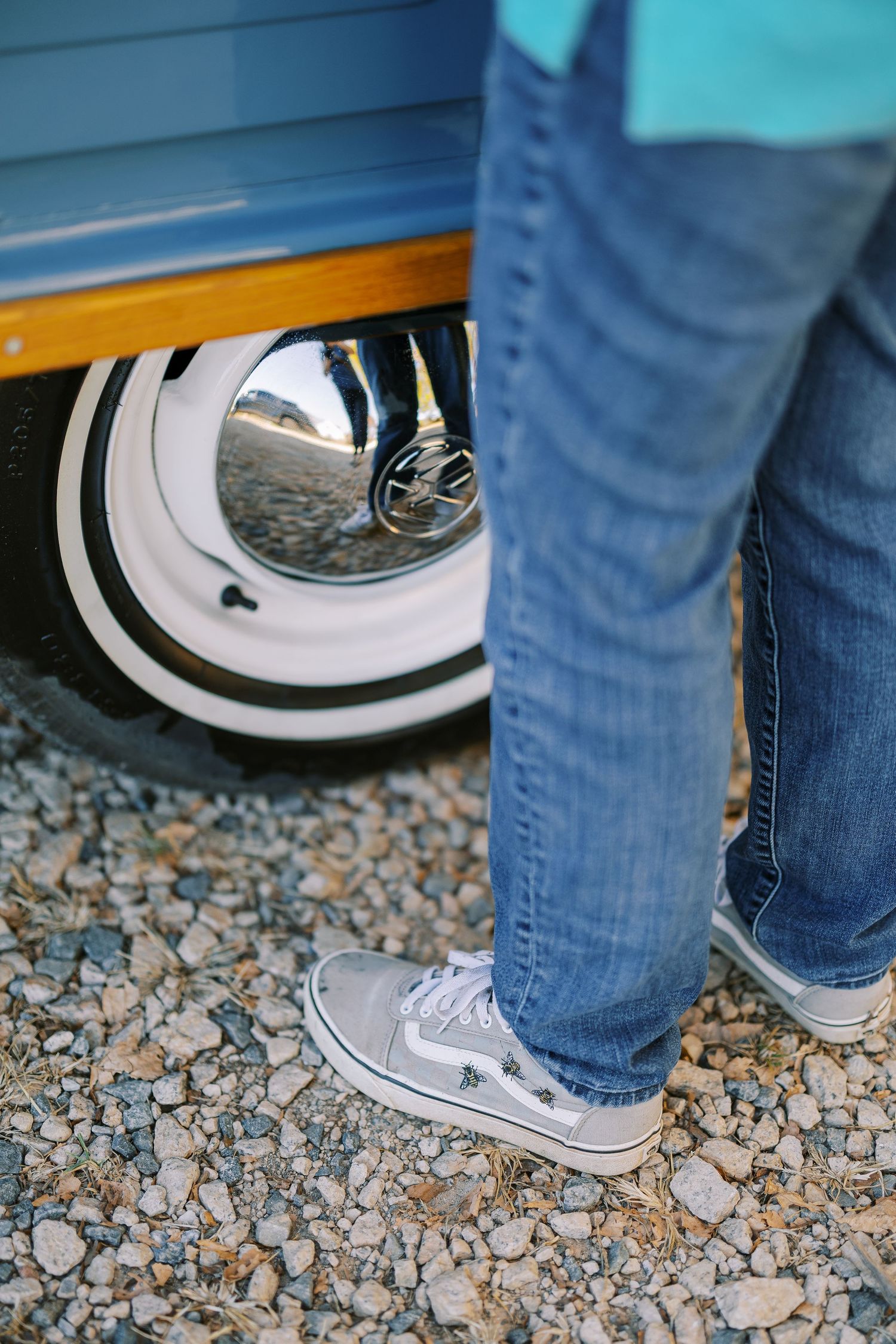 Close-up view of people wearing blue jeans and white sneakers standing on gravel ground.