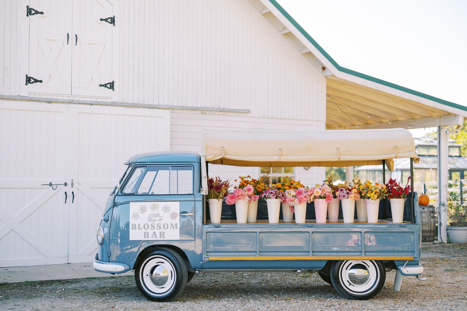 A vintage blue Ford station wagon with wood paneling sits parked in front of a white building with colorful flowers.