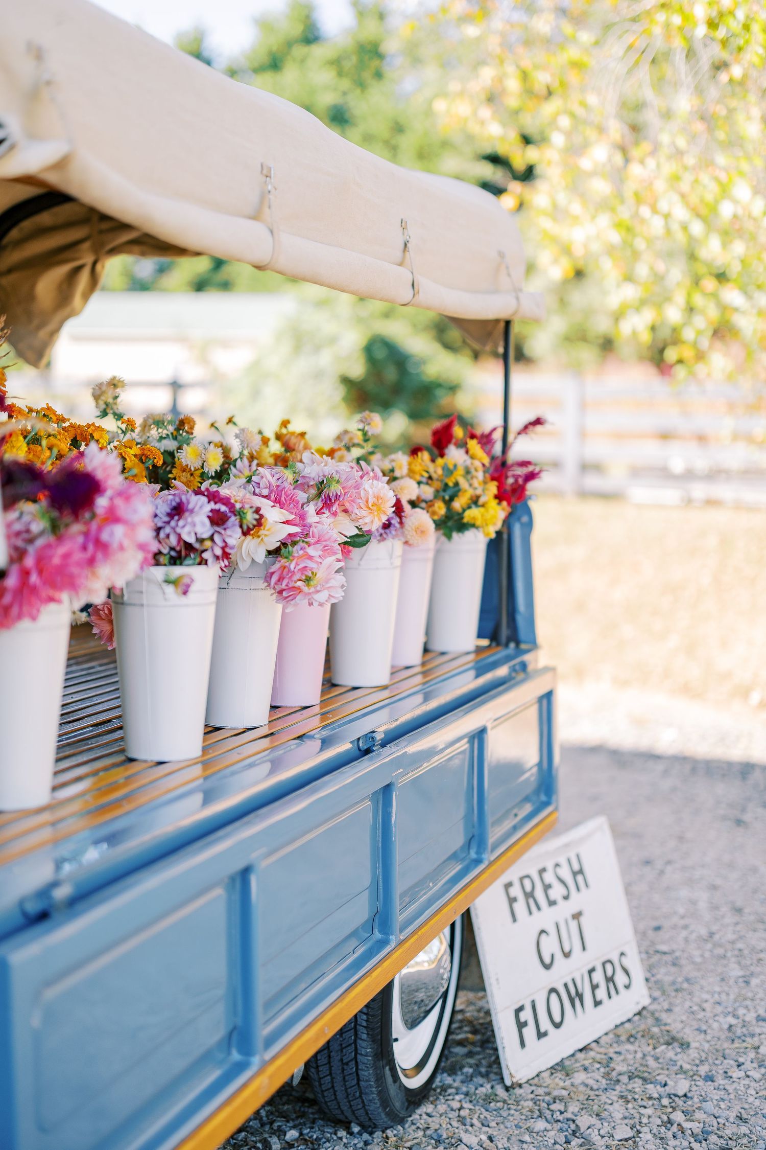 White buckets filled with colorful fresh cut flowers displayed on a blue painted cart with a rustic sign.