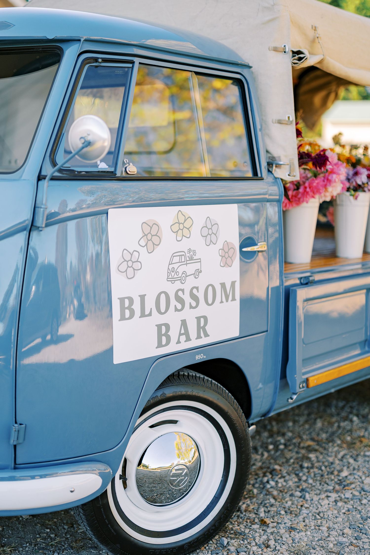 A vintage blue Volkswagen van with 'Blossom Bar' signage displayed at an outdoor event.