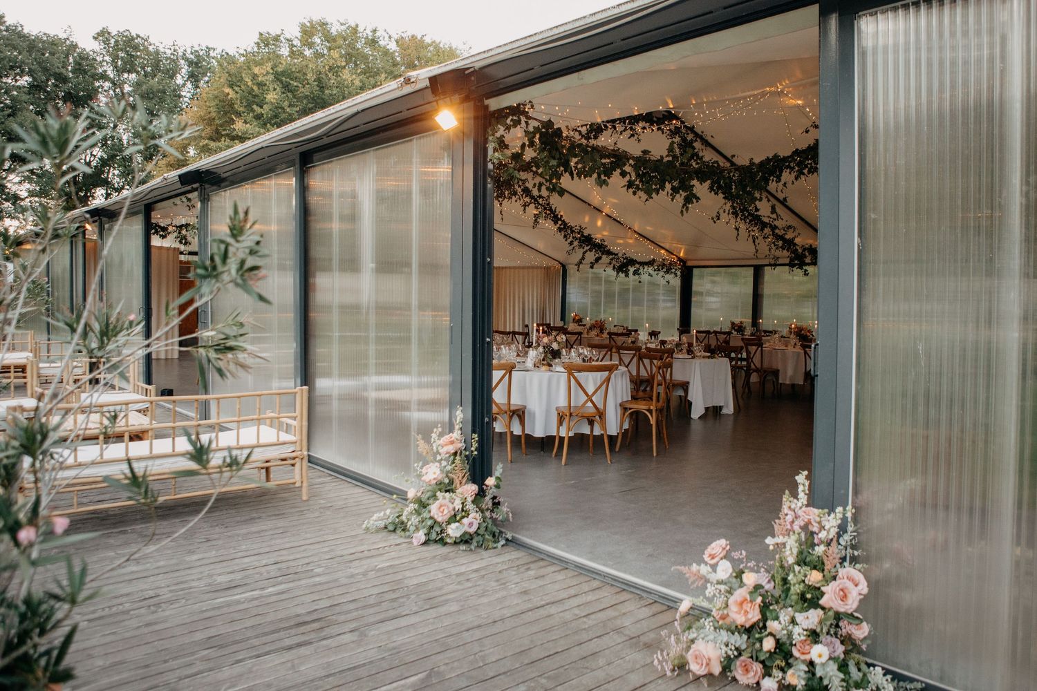Modern glass wedding reception venue with open sliding doors and pink floral entrance decorations.