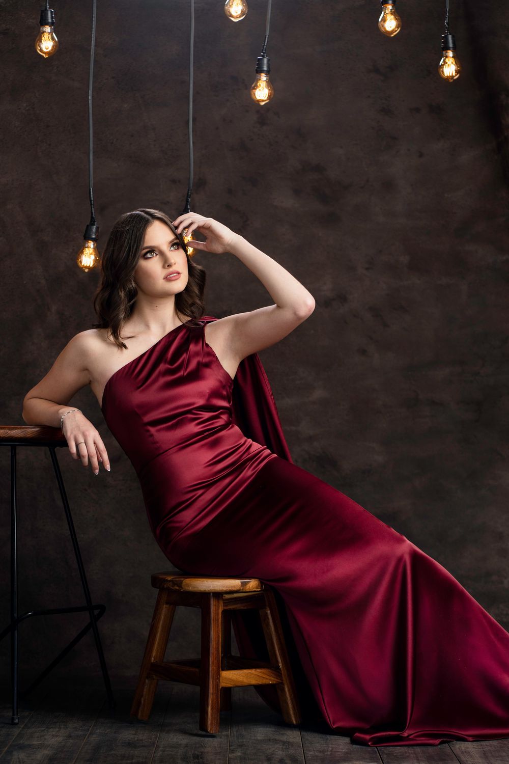 Elegant photoshoot in burgundy dress with moody lighting and wooden chair.