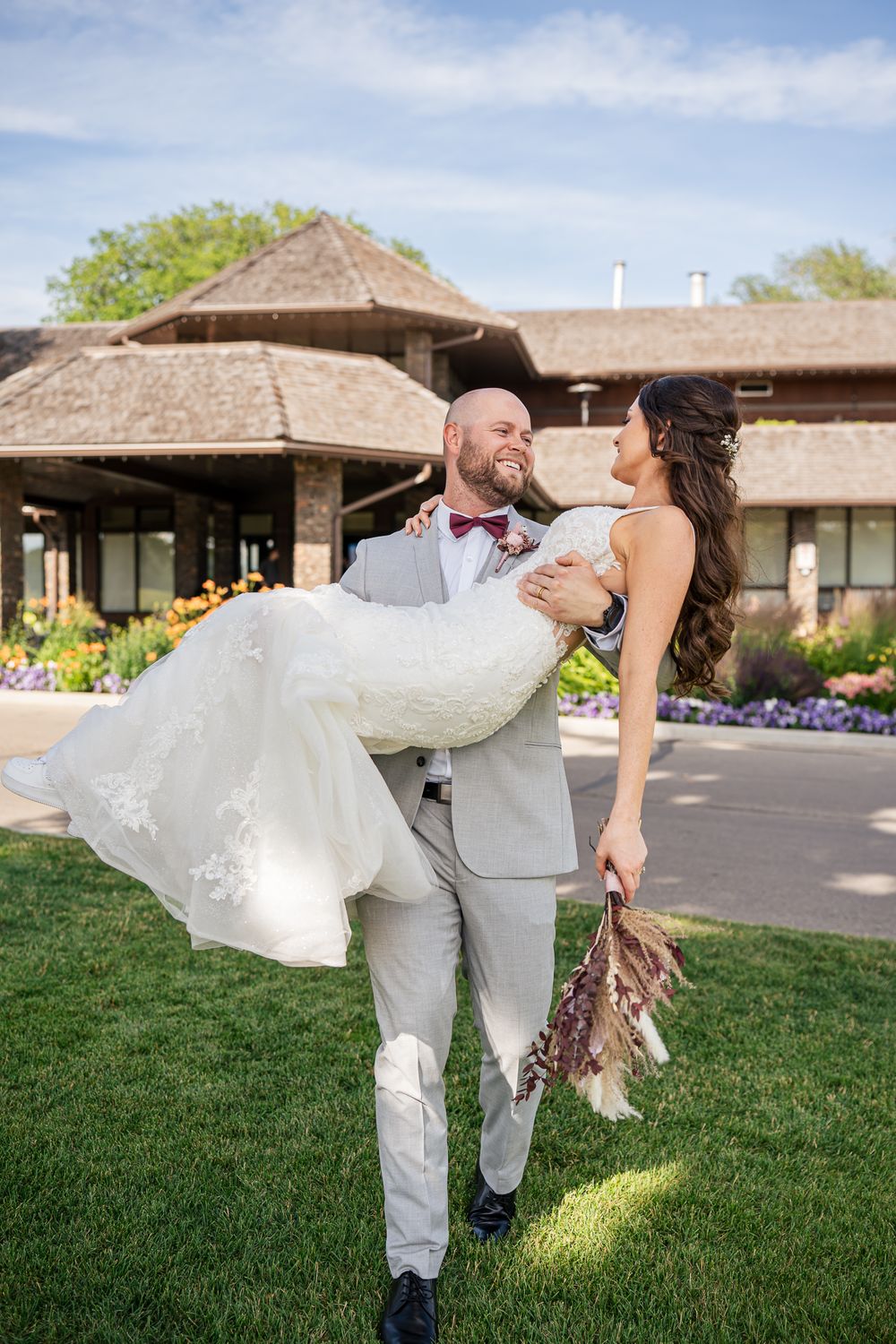 Couple at outdoor venue on wedding day with flowers in background and elegant building with thatched roof.