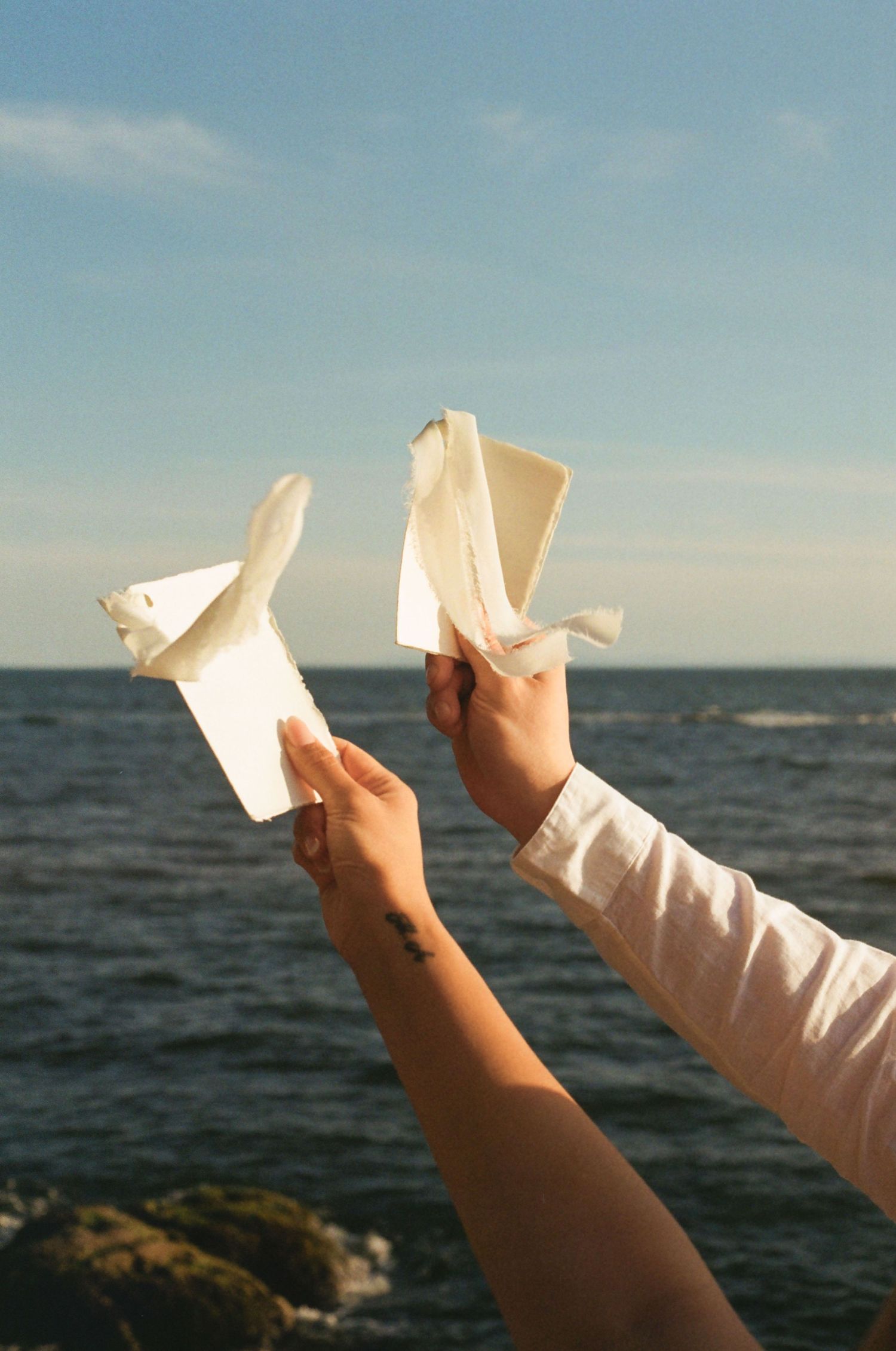 Hands releasing paper planes into the sky over an ocean horizon at sunset, creating a sequence of launch moments.