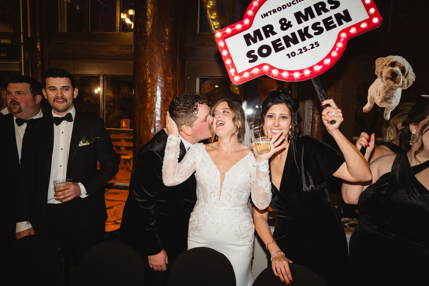 Wedding guests dance and celebrate on a dimly lit dance floor at an evening reception.