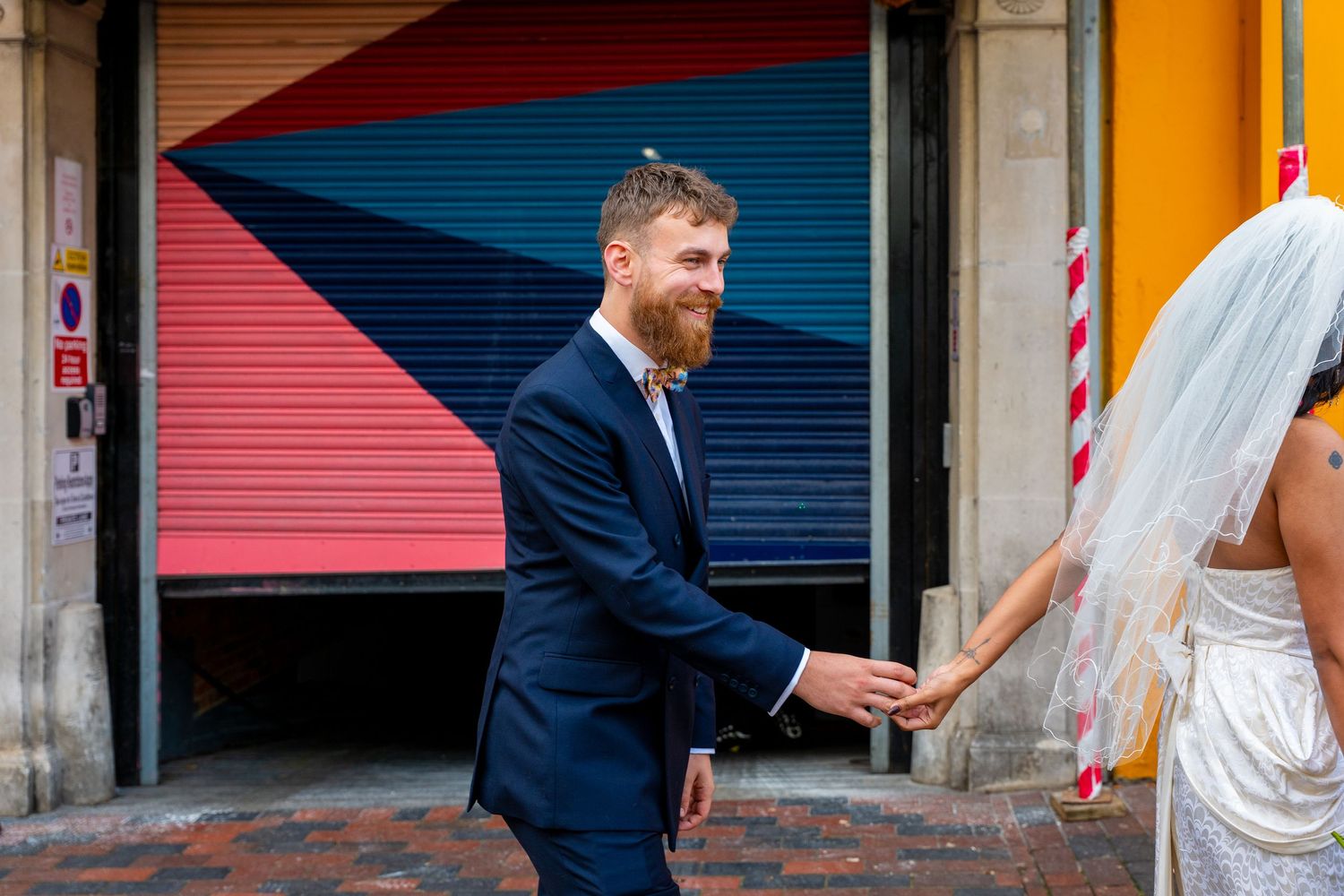 Newlywed couple shares a joyful moment outside colorful shuttered storefronts during their wedding photoshoot.