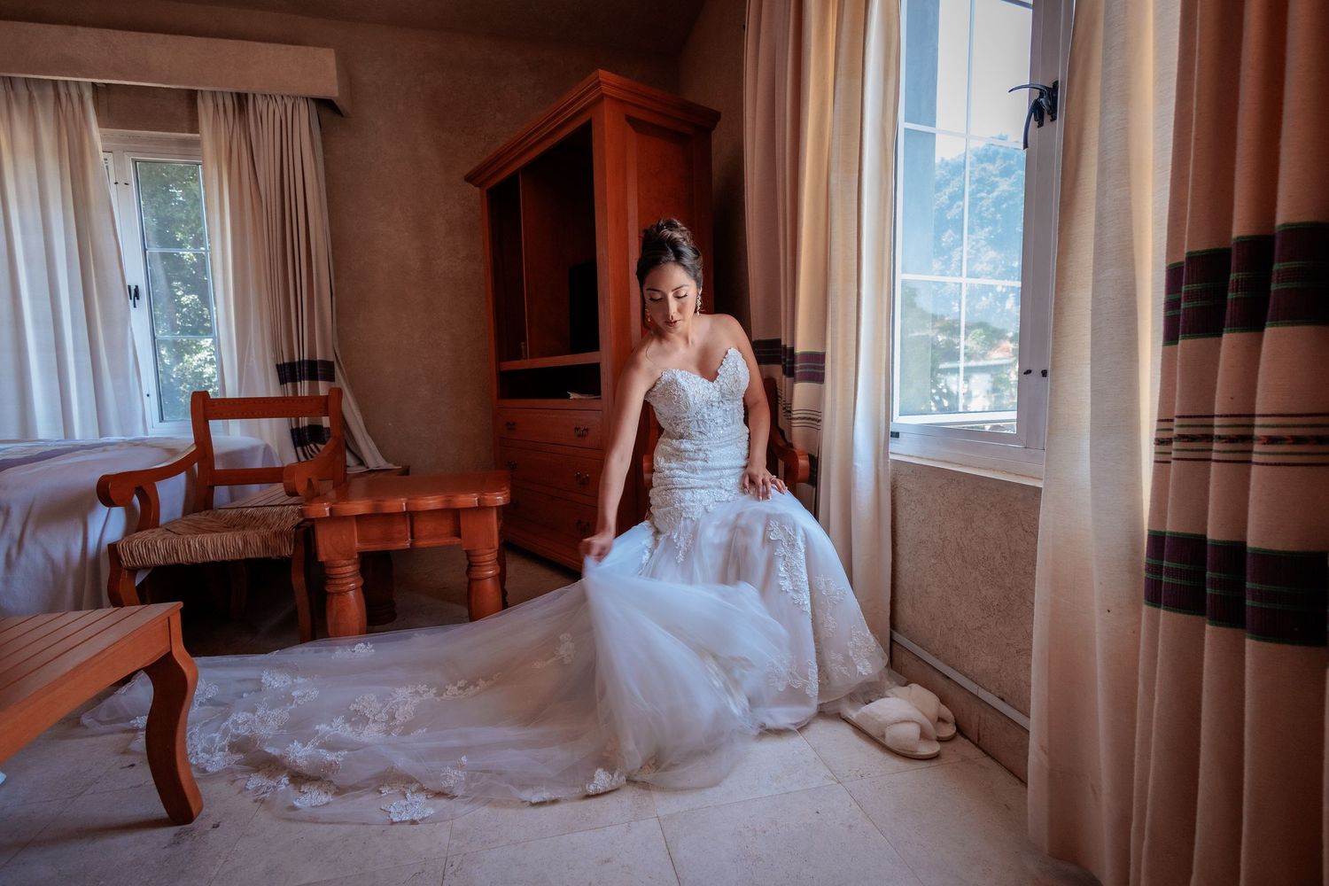Wedding dress displayed in an empty room with sunlight casting shadows through curtains.