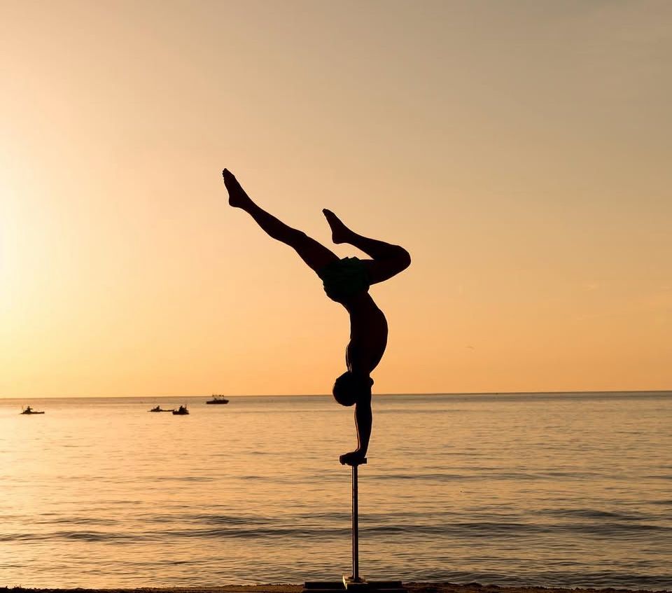 Silhouettes of people doing handstands and acrobatics on beach at golden hour.