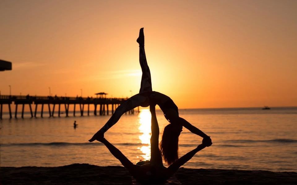 Silhouetted figures performing gymnastic poses against dramatic ocean sunset.