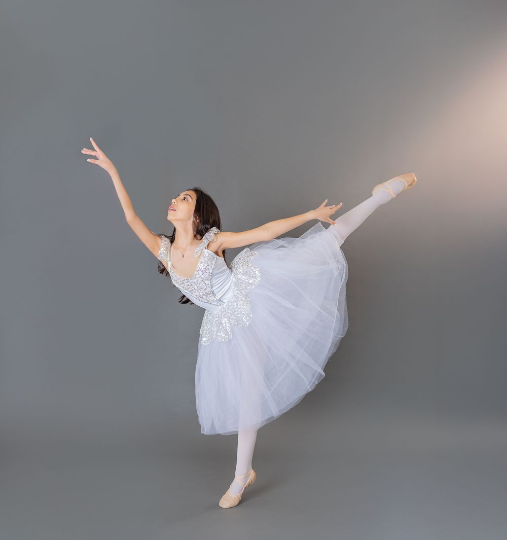 A graceful ballet dancer in a white tutu performs a series of elegant arabesque poses against a gray backdrop.