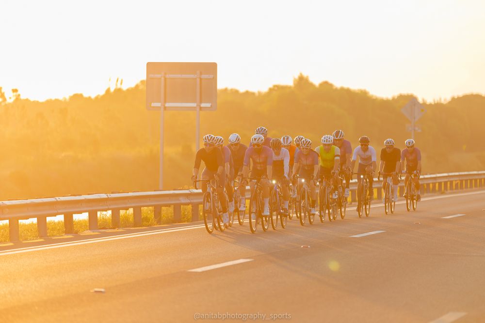 Cyclists riding together on a road during golden hour sunset with long shadows cast on the pavement.
Sports photography.