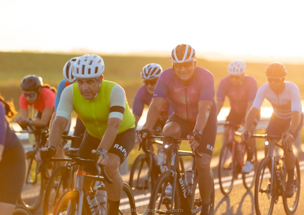Group of cyclists pedaling in formation along a road at sunset with warm golden light.
Sports photography.