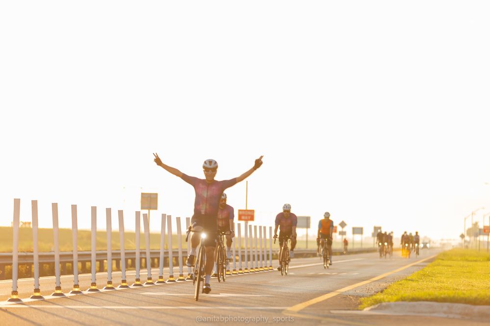 Cyclists silhouetted against a bright sunset sky while riding on a barrier-lined road.
Sports photography.