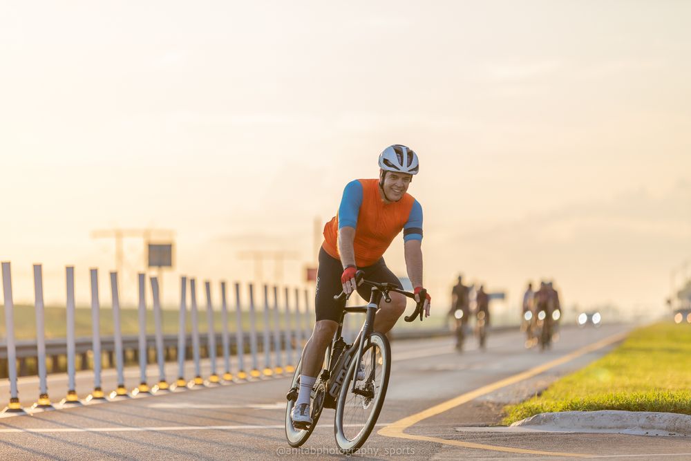 Road cyclists training together on a paved path during sunset with safety barriers visible.
Sports photography.