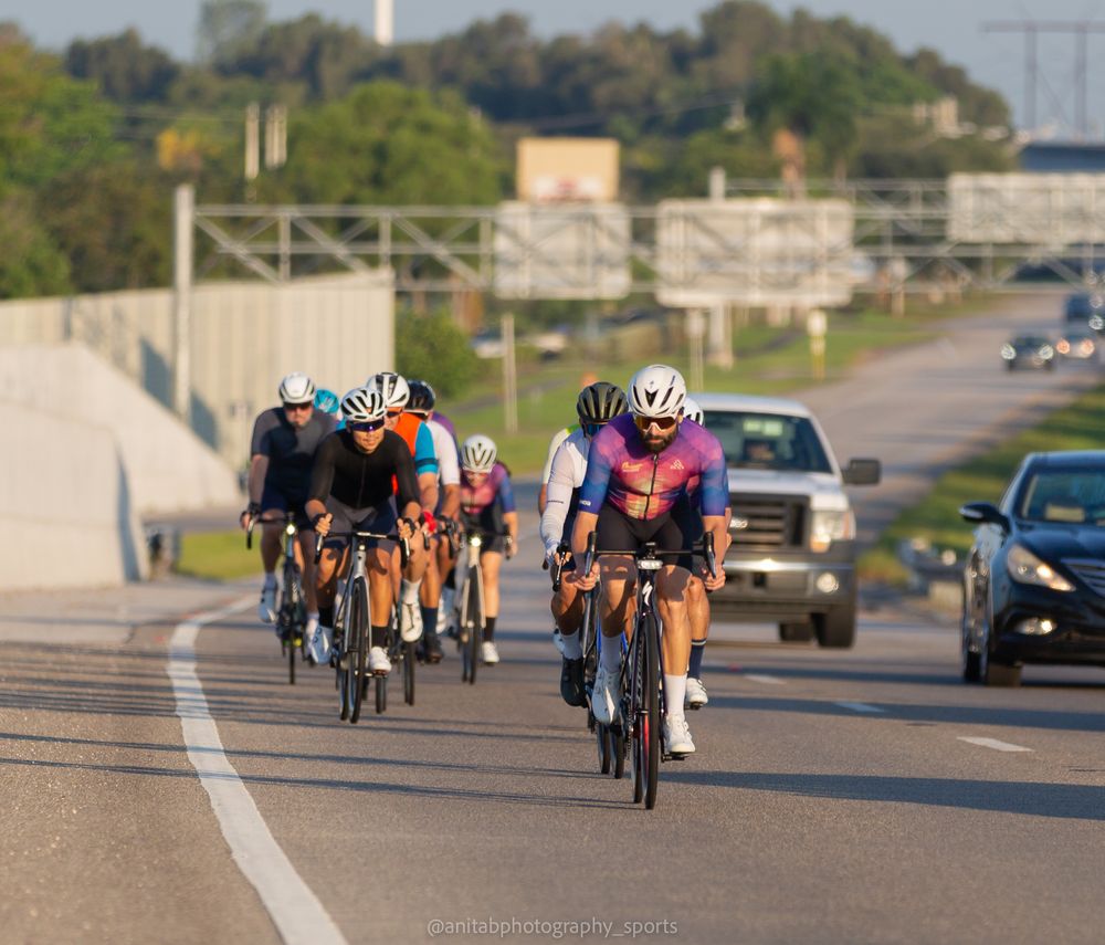 Cyclists riding on a suburban road with trees and buildings visible in the background.
Sports photography.