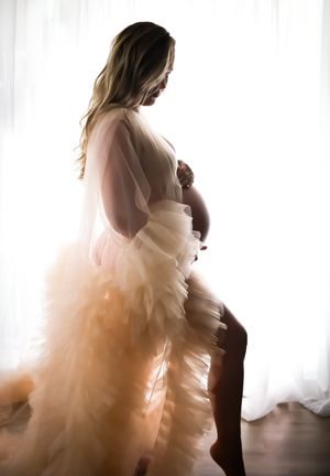 Backlit maternity portraits with ethereal tulle dress creating a romantic silhouette.