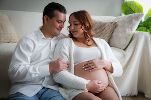 Intimate maternity moment captured on cozy white couch with couple in matching white sweaters.