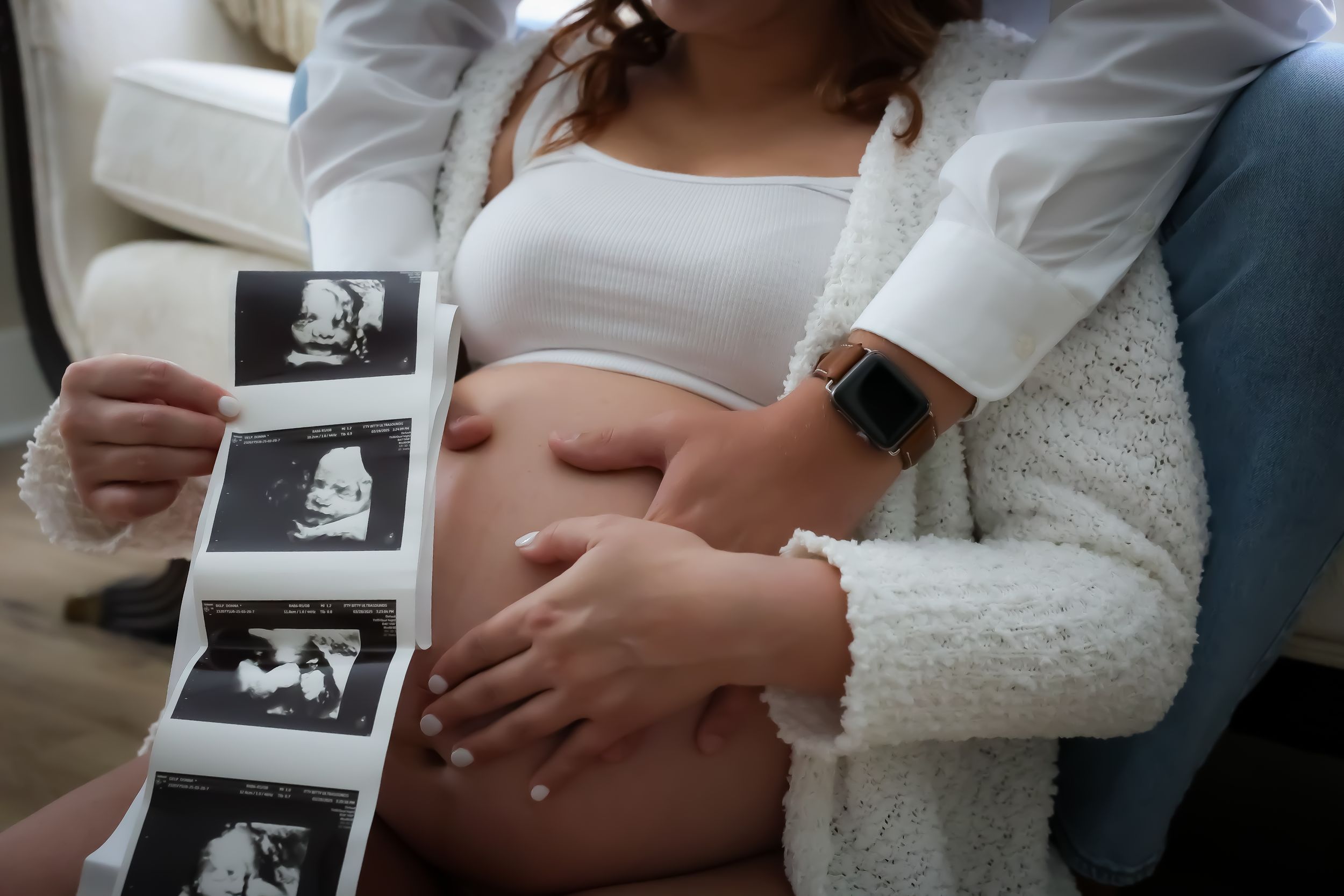 Close-up of ultrasound photos being held against pregnant belly.