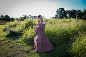 A maternity photo in a sunlit meadow with tall grass and wildflowers.