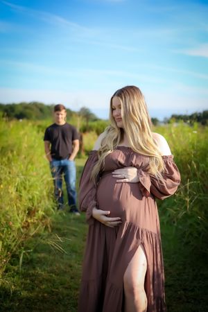 A romantic maternity photoshoot in a sunny meadow with tall grass.