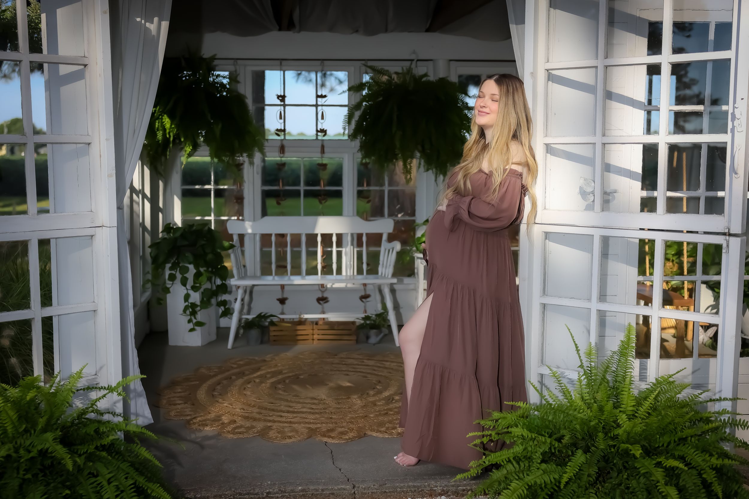 A maternity photo in a white gazebo surrounded by hanging plants.