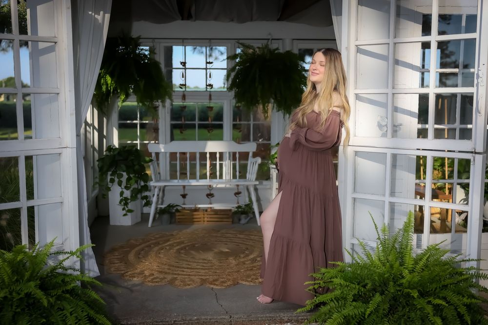 A maternity photo in a white gazebo surrounded by hanging plants.