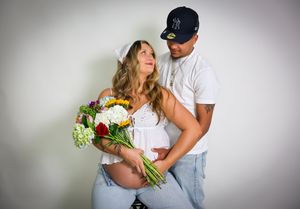 A casual maternity photo with white flowers against a grey background.