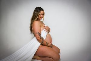 Artistic maternity photo with flowing white fabric against grey backdrop.