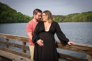 Romantic maternity photo of couple on wooden dock overlooking serene lake.