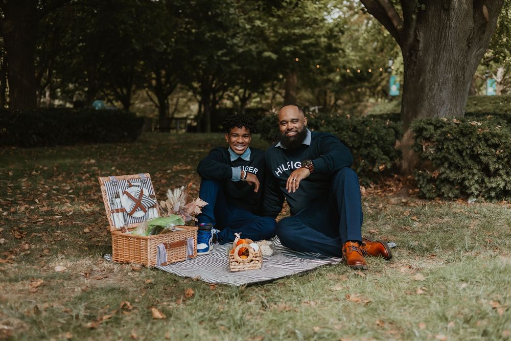 A group enjoys a cozy autumn picnic spread on a blanket under trees in a park setting.