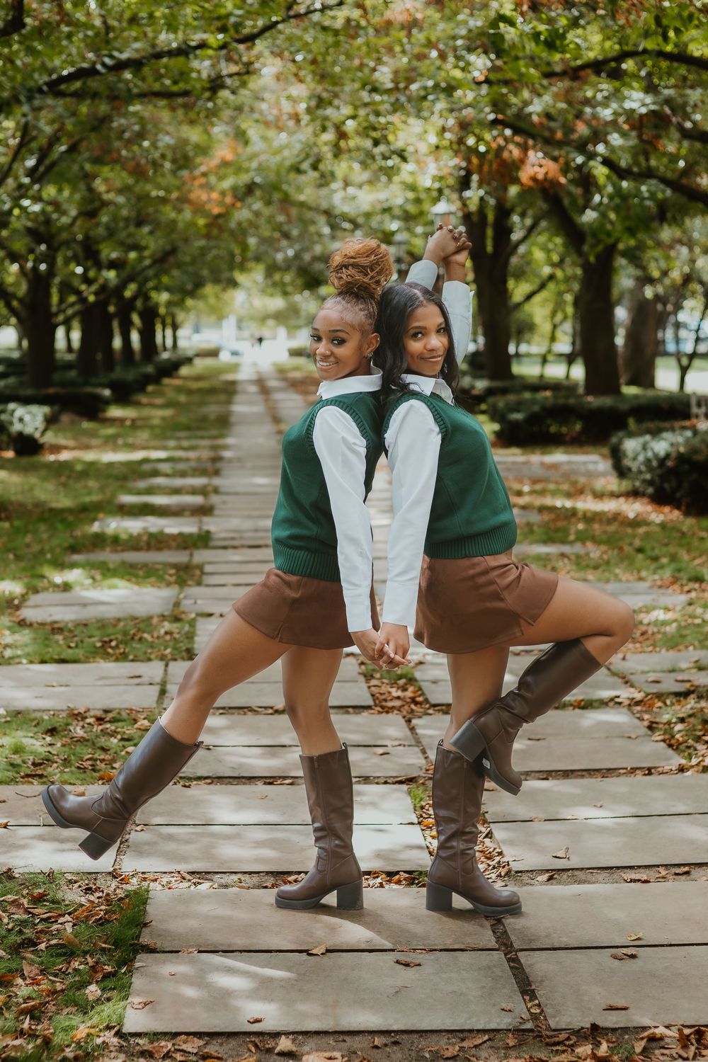 Autumn fashion details showing brown knee-high boots and green outfits on a stone path with fallen leaves.