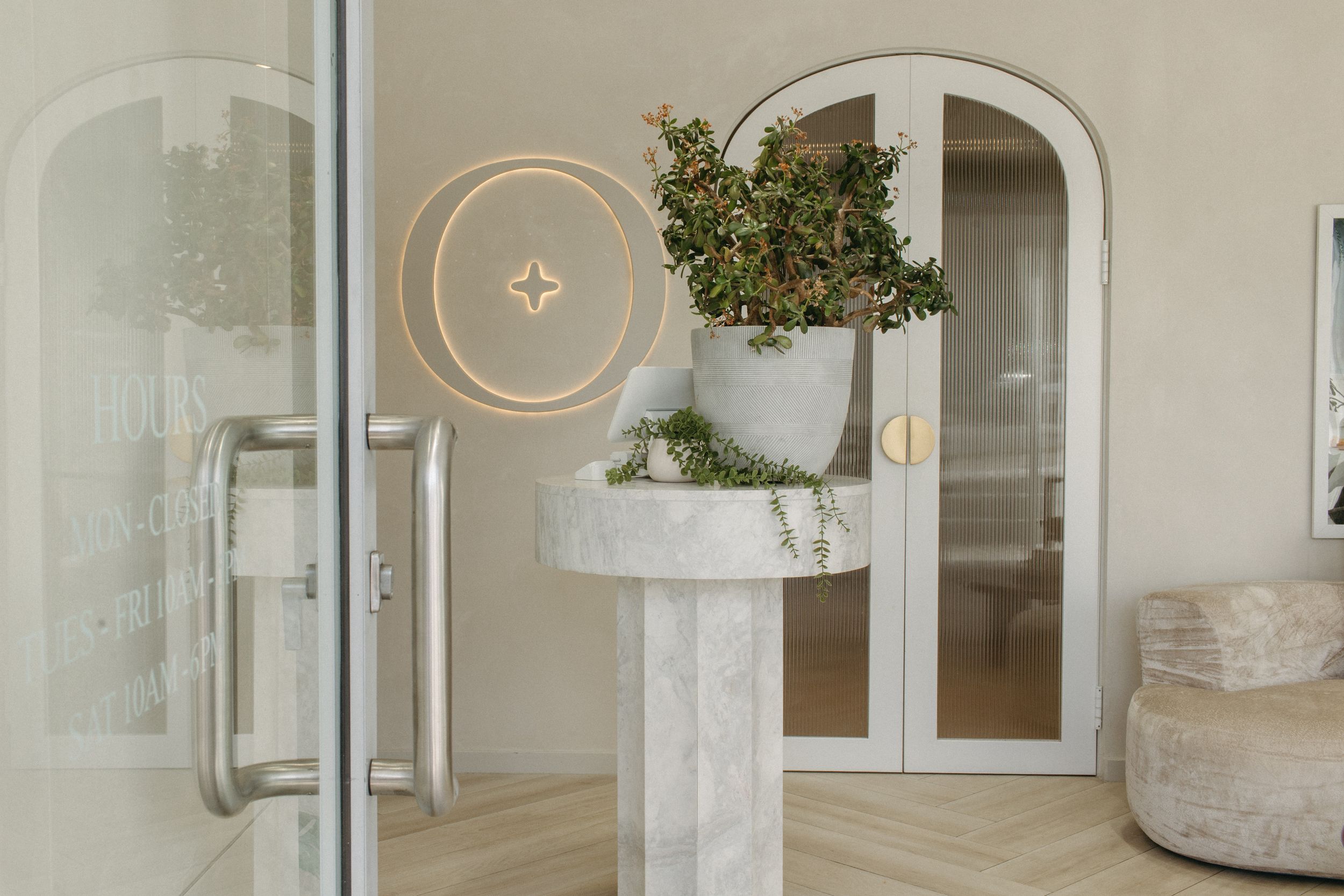 Elegant marble pedestal with a lush green plant in a white pot, arched glass doors, and a gold circular wall light.