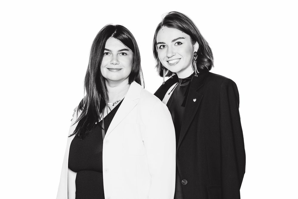 Professional black and white photo of two women standing together against a white background.