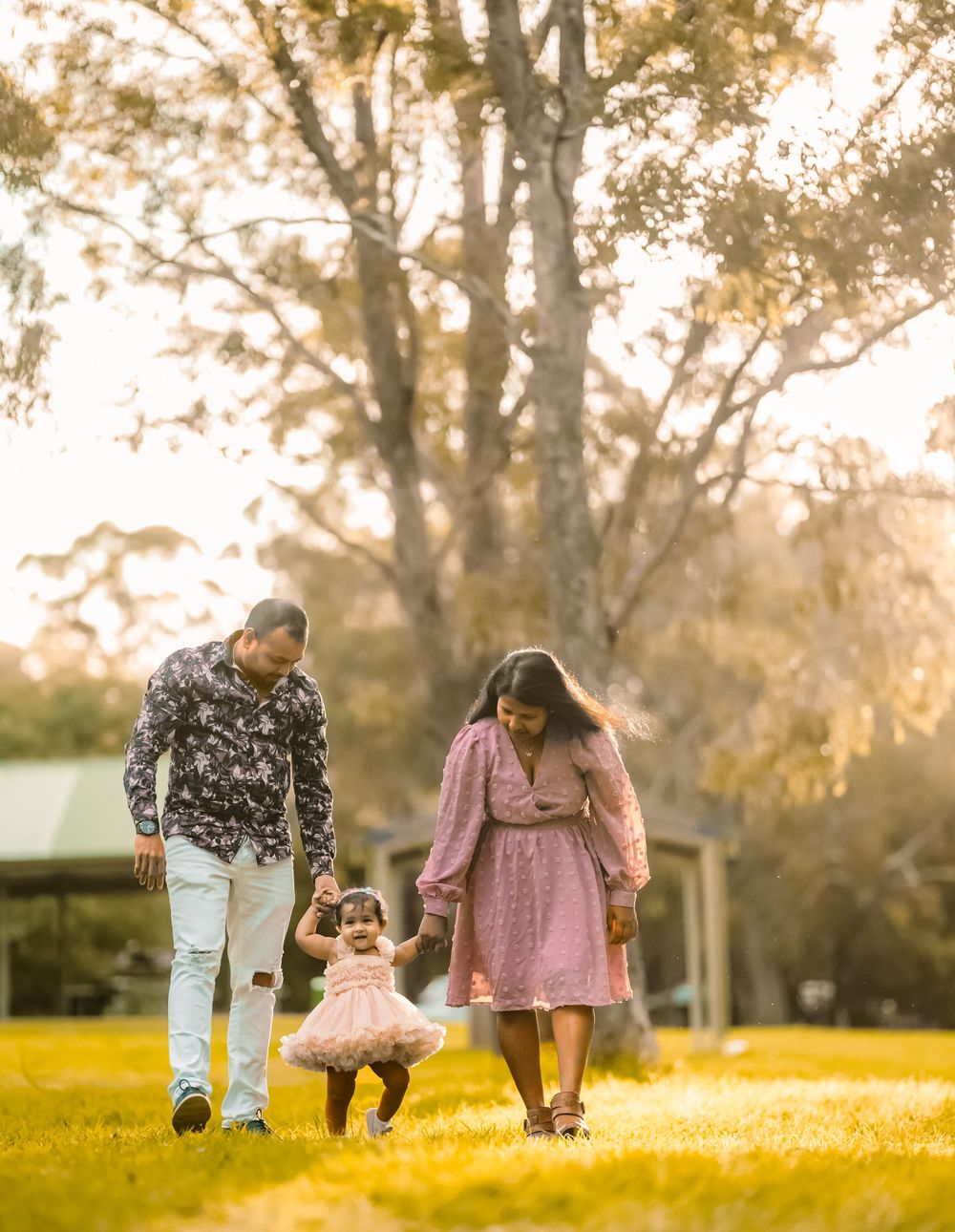 Family walking together in a park during golden sunset hour with sunlight filtering through autumn trees.