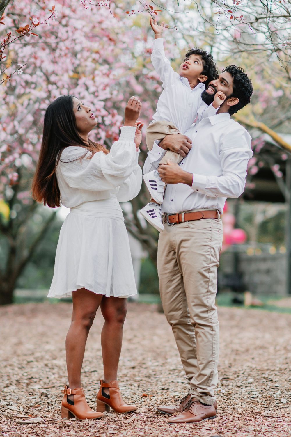 A couple in white and beige outfits dance playfully under blooming cherry blossom trees in a romantic spring photoshoot.