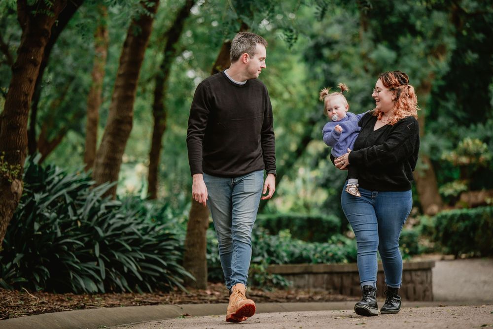 A family walks together on a garden path surrounded by lush greenery and trees.