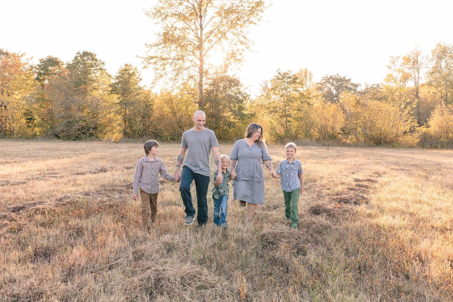 Family walking together through golden field during sunset photo session.