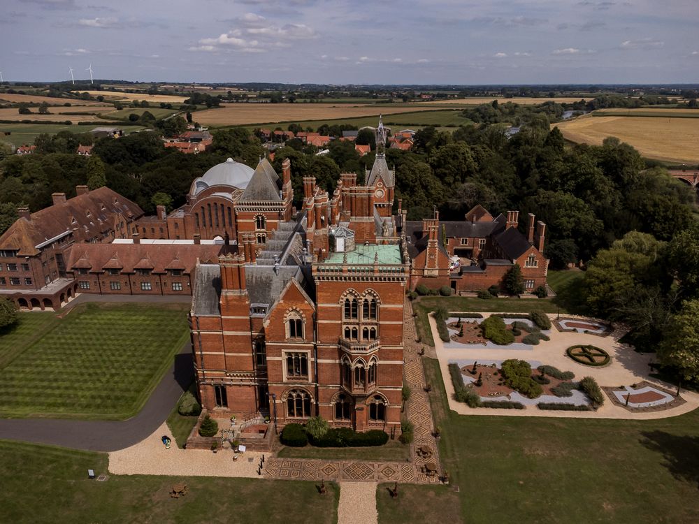 Drone shot of a magnificent red brick manor house with formal gardens and surrounding countryside.