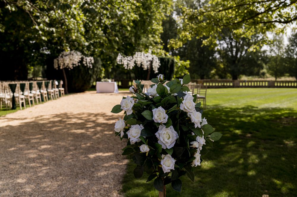Outdoor wedding ceremony setup with white floral arrangements and hanging decorations in a garden setting.