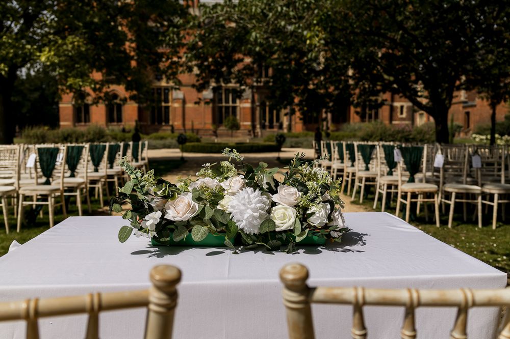 Elegant table setting with white floral centerpiece and gold chairs for an outdoor wedding reception.