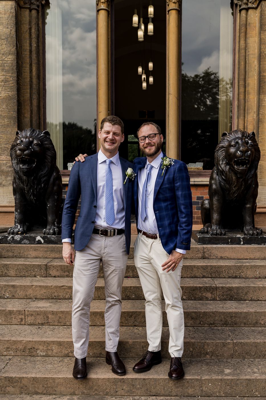 A wedding photo on stone steps with decorative lion statues and hanging lights in an elegant architectural setting.