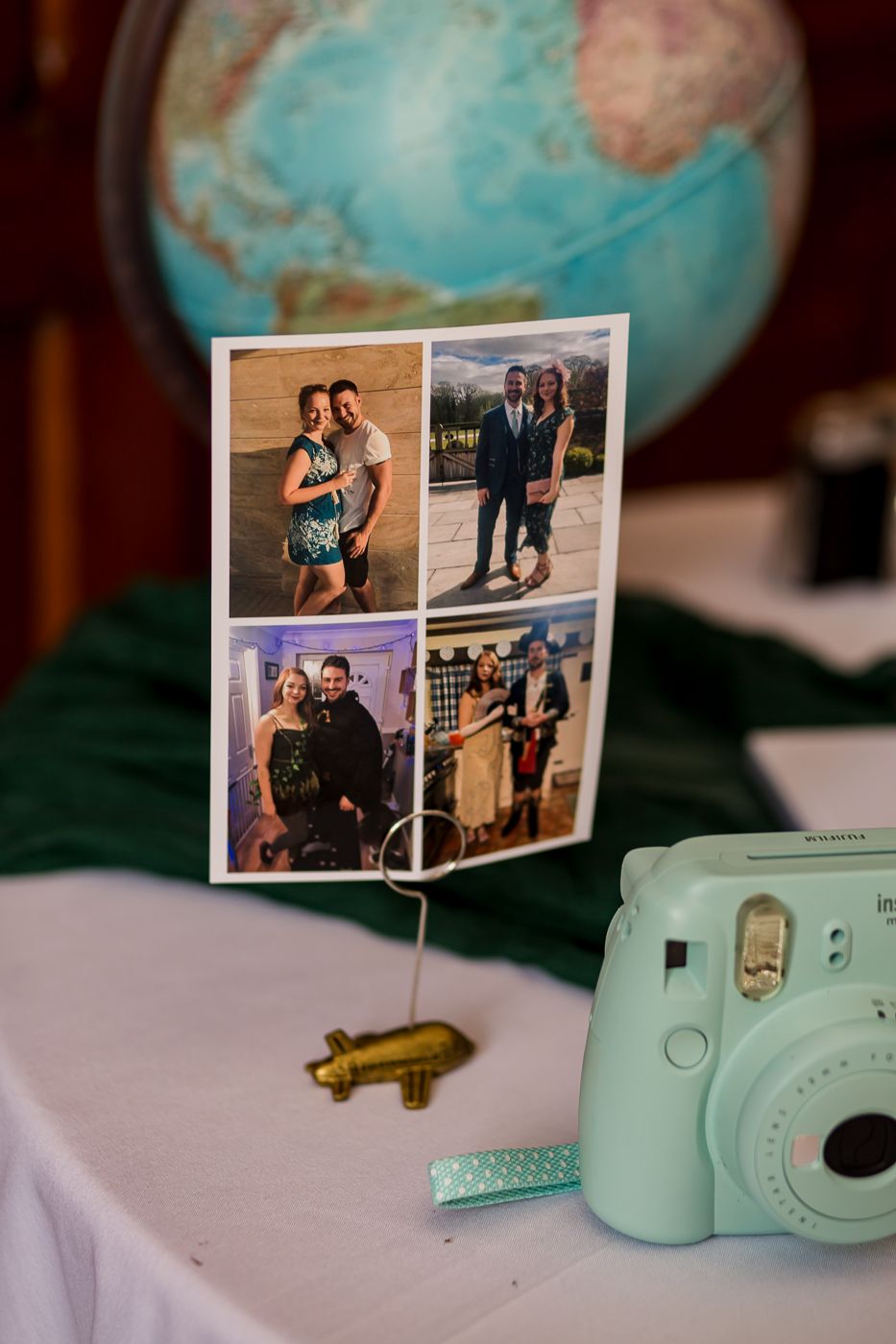 A photo display with a globe and mint green Instax camera on a white tablecloth.