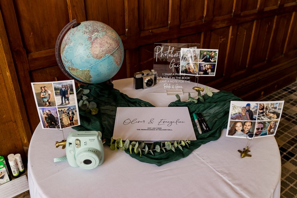 Wedding decor featuring a vintage globe, Instax camera, and photo displays on a white-clothed table.