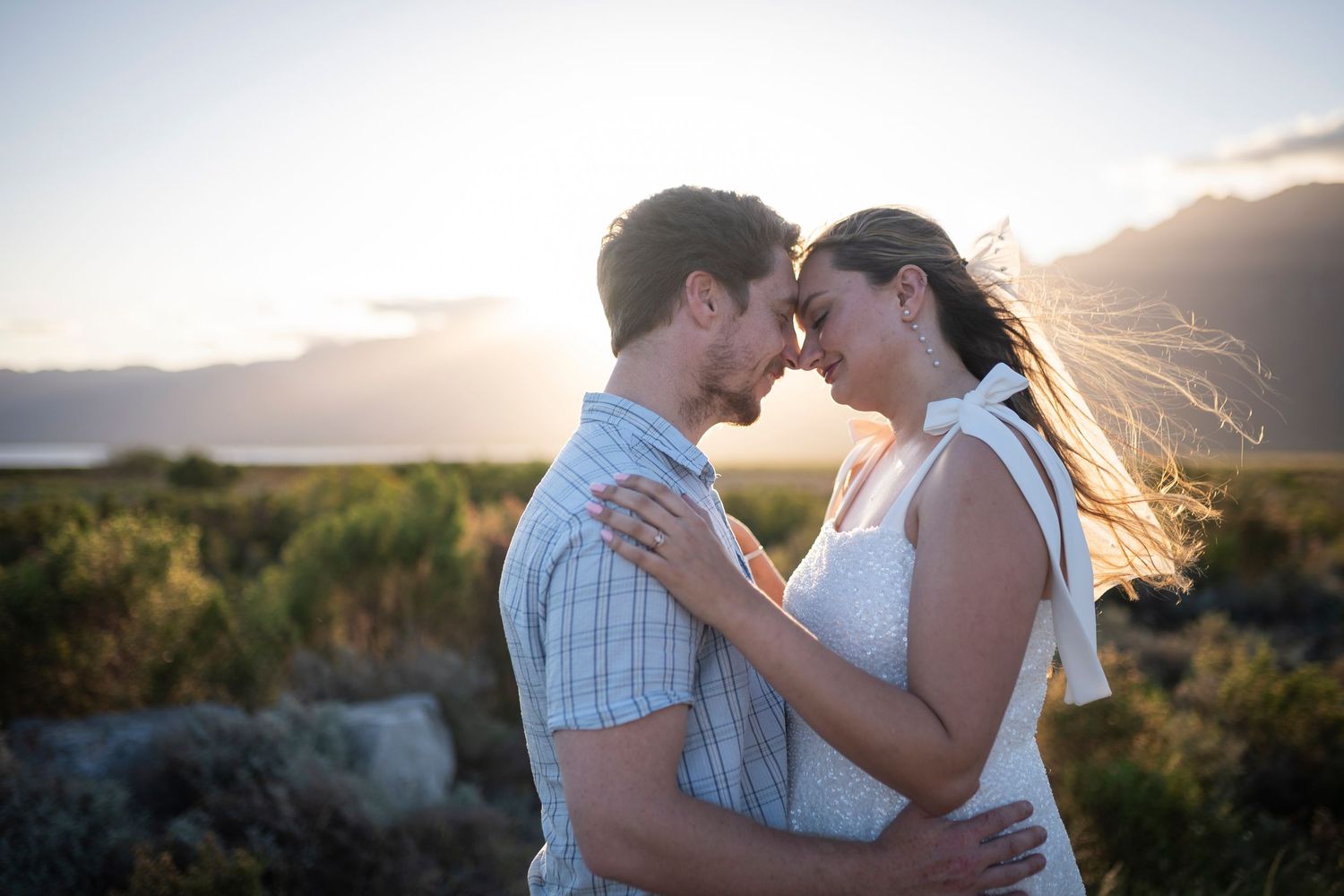 A romantic couple embraces during golden hour with sunlight streaming through their hair in a natural outdoor setting.