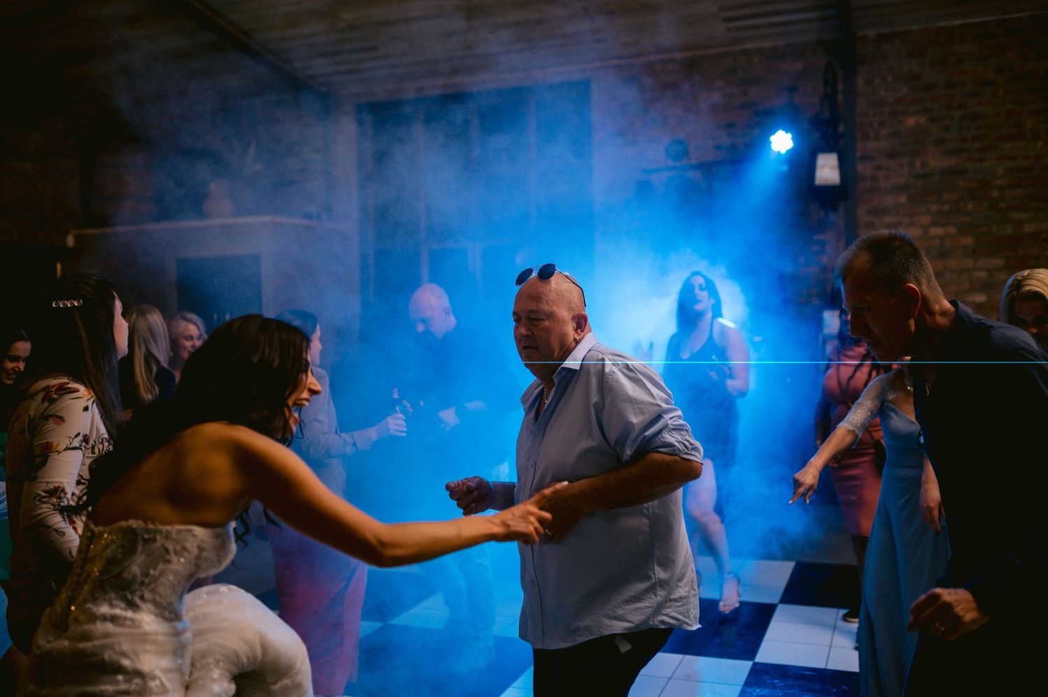 Couples dance together in a dimly lit ballroom with dramatic blue lighting creating an atmospheric mood.