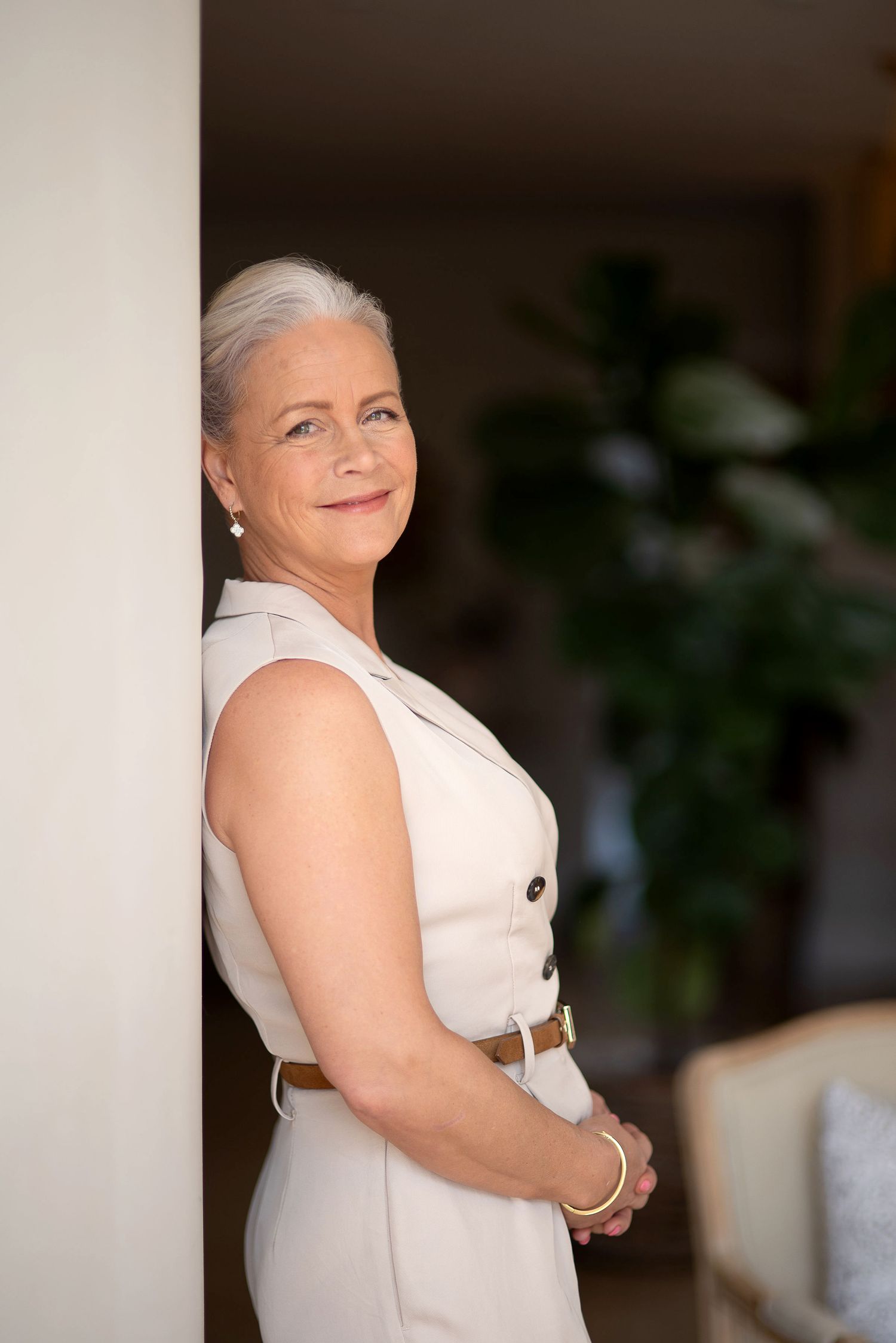 Person in a sleeveless white dress smiles while posing against a blurred indoor background.
