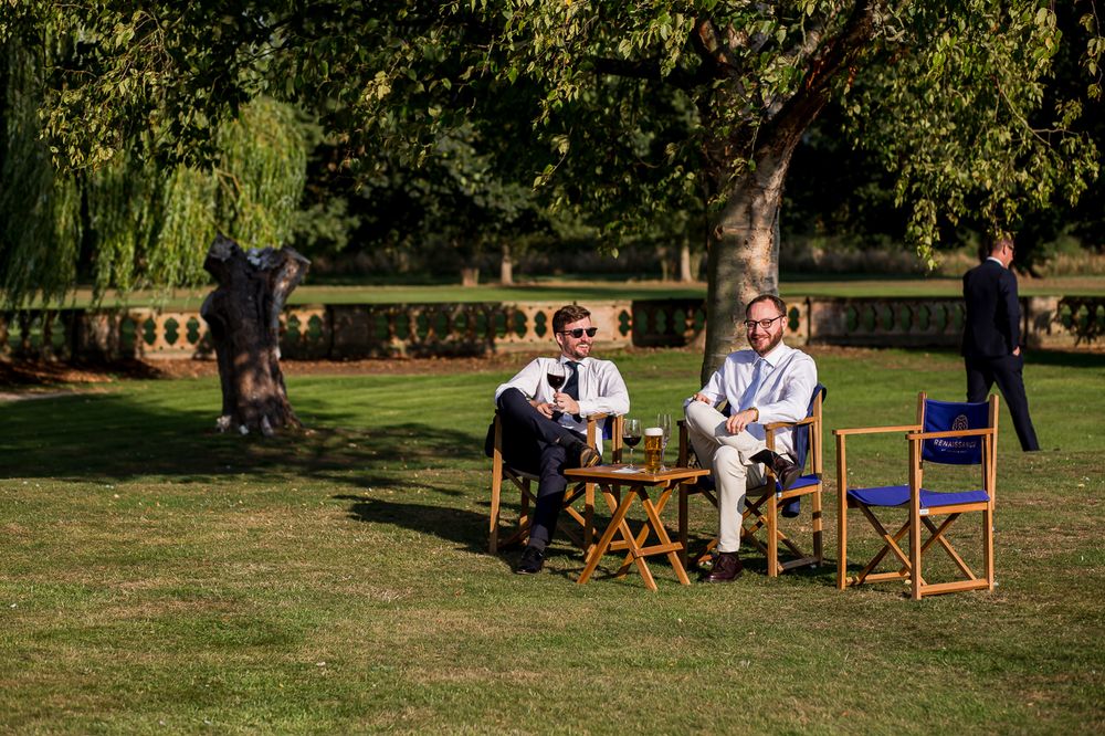 Wedding guests relaxing in chairs on a sunny lawn with trees in the background.