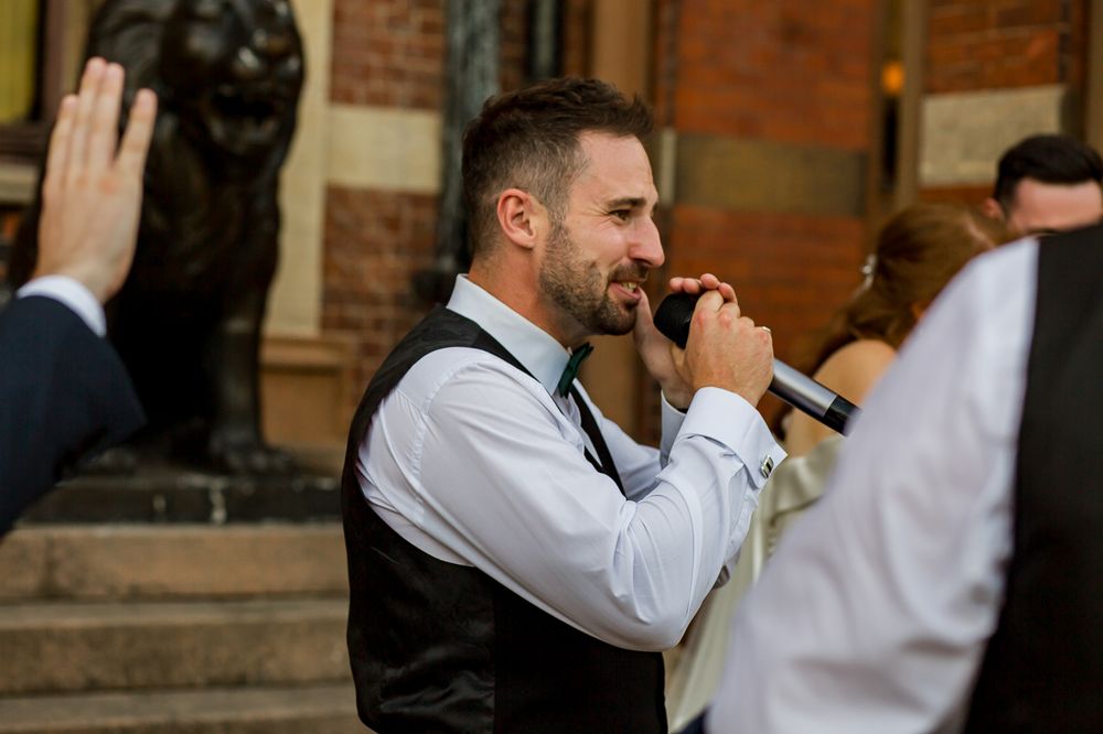 Wedding performer singing passionately into microphone on outdoor steps.